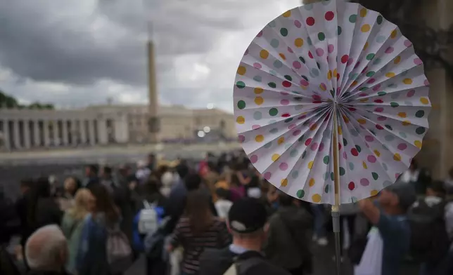 A guide uses a colourful hand fan to lead the group as they leave after viewing Pope Francis lying in state inside St. Peter's Basilica,, at the Vatican, Friday, April 25, 2025. (AP Photo/Andrew Medichini)