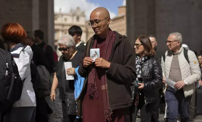 A pilgrim holds a picture of Pope Francis as he waits in line to view Pope Francis lying in state inside St. Peter's Basilica, at the Vatican, Friday, April 25, 2025. (AP Photo/Francisco Seco)