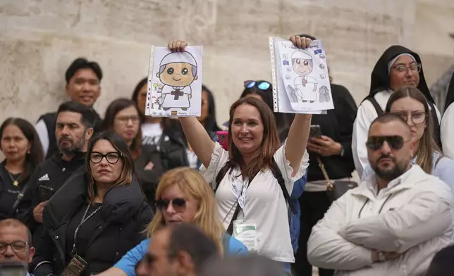 A woman holds drawings depicting the pontiff as people wait in St. Peter's Square to pay their respects to the late Pope Francis, lying in state at St. Peter's Basilica for the final day, at the Vatican, Friday, April 25, 2025. (AP Photo/Andreea Alexandru)