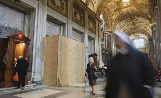 People walk past a wooden board where work in progress is taking place on the spot where Pope Francis will be buried, inside St. Mary Major basilica, in Rome, Tuesday, April 22, 2025. (AP Photo/Alessandra Tarantino)