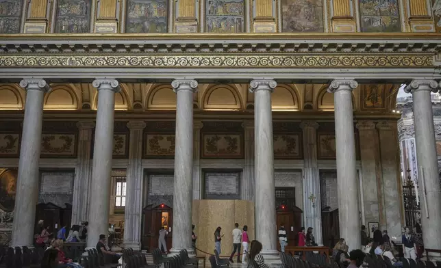 People walk past a wooden board where work in progress is taking place on the spot where Pope Francis will be buried, inside St. Mary Major basilica, in Rome, Tuesday, April 22, 2025. (AP Photo/Alessandra Tarantino)