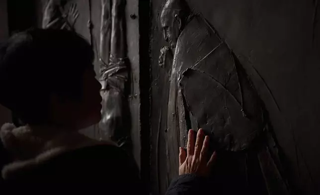 A woman places her hand on the entrance door of St. Peter's Basilica where Pope Francis lying in state, at the Vatican, Friday, April 25, 2025. (AP Photo/Emilio Morenatti)