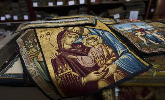 A religious tapestry is displayed in a shop as Pope Francis is lying in state inside St. Peter's Basilica , at the Vatican, Friday, April 25, 2025. (AP Photo/Bernat Armangue)