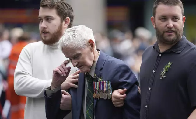 A veteran, center, is assisted as they march past thousands of people lining the street to pay tribute to their war dead during the Anzac Day parade in Sydney, Australia, Friday, April 25, 2025. (AP Photo/Rick Rycroft)