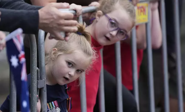 Sage Smith, 5, left, and her six-year-old sister Hazel, peer through a gate while waiting for participants to march by as thousands of people line the street to pay tribute to their war dead during the Anzac Day parade in Sydney, Australia, Friday, April 25, 2025. (AP Photo/Rick Rycroft)
