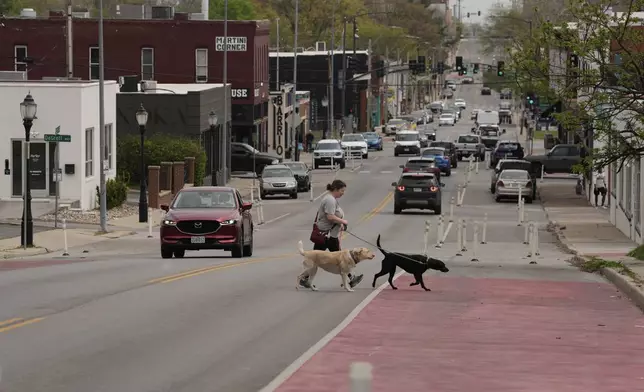 A woman and her dogs cross 31st Street in Kansas City, Mo., where the city implemented a "road diet" reducing the street from four lanes to two in an effort to reduce speeding and accidents, Thursday, April 17, 2025. (AP Photo/Charlie Riedel)