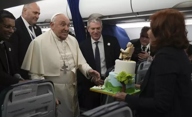 FILE - Pope Francis is presented with a cake by Valentina Alazraki, correspondent for TeleVisa Univision, to celebrate his upcoming Dec. 17, 88th birthday, on the flight back to Rome at the end of his one-day visit to Ajaccio in the French island of Corsica, Sunday, Dec. 15, 2024. (AP Photo/Alessandra Tarantino, Pool, File)
