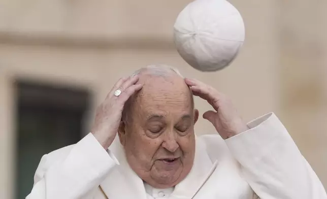 FILE - Pope Francis tries to catch his cap as wind blows it away while arriving for his weekly general audience in St. Peter's Square at the Vatican, Wednesday, March 13, 2024. (AP Photo/Andrew Medichini, File)