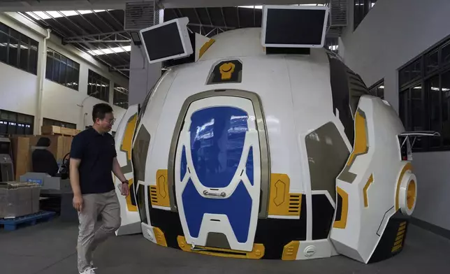 A worker past by a virtual reality experience platform built at the factory of Zhuoyuan Tech Co., Ltd in Panyu district of Guangzhou city in southern China's Guangdong province on Wednesday, April 16, 2025. (AP Photo/Ng Han Guan)
