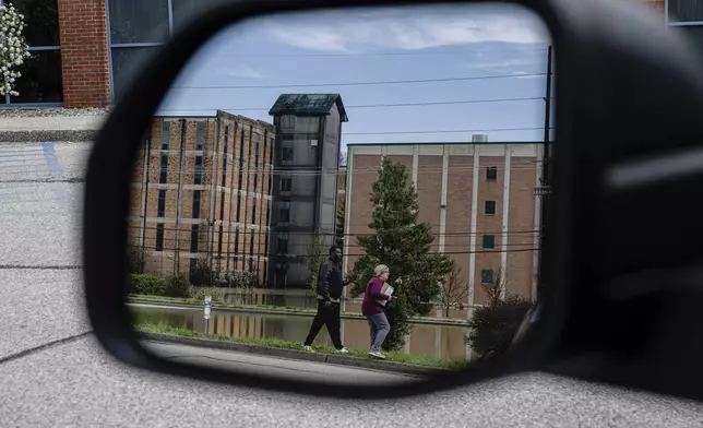 In a reflection, community members walk near the flooded Buffalo Trace Distillery on Monday, April 7, 2025, in Frankfort, Ky. (AP Photo/Jon Cherry)