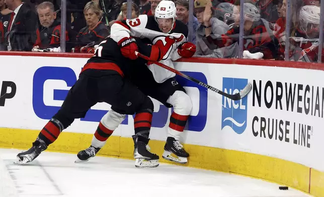 New Jersey Devils' Jesper Bratt (63) is checked into the board by Carolina Hurricanes' Jalen Chatfield (5) during the first period of Game 1 of an NHL hockey Stanley Cup first-round playoff series in Raleigh, N.C., Sunday, April 20, 2025. (AP Photo/Karl DeBlaker)