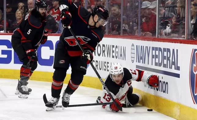 New Jersey Devils' Nico Hischier (13) battles for the puck with Carolina Hurricanes' Dmitry Orlov (7) during the first period of Game 1 of an NHL hockey Stanley Cup first-round playoff series in Raleigh, N.C., Sunday, April 20, 2025. (AP Photo/Karl DeBlaker)