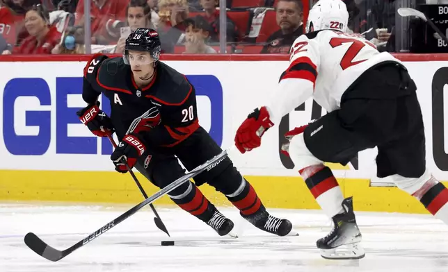 Carolina Hurricanes' Sebastian Aho (20) carries the puck to challenge New Jersey Devils' Brett Pesce (22) during the second period of Game 1 of an NHL hockey Stanley Cup first-round playoff series in Raleigh, N.C., Sunday, April 20, 2025. (AP Photo/Karl DeBlaker)