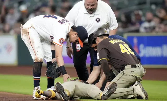San Diego Padres' Luis Arraez lies on the ground after a collision with with Houston Astros second baseman Mauricio Dubon, left, as Padres first base coach David Macias (46) along with an Astros' trainer check on him at first base during the first inning of a baseball game Sunday, April 20, 2025, in Houston. (AP Photo/Karen Warren)