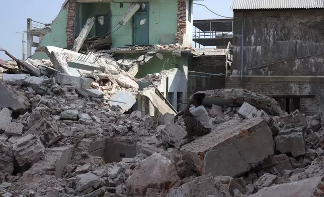 A volunteer sits collapsed building after one month of the strong earthquake, in Naypyitaw, Myanmar, Monday, April 28, 2025. (AP Photo/Aung Shine Oo)