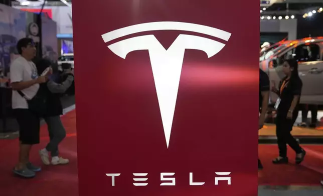 People pass by a Tesla sign at the Manila International Auto Show in Pasay city, Philippines Friday, April 11, 2025. (AP Photo/Aaron Favila)