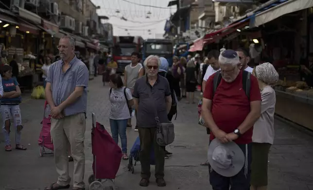 People stand still during a two-minute siren marking the annual Israeli Holocaust Remembrance Day at the Mahane Yehuda market, in Jerusalem, Thursday, April 24, 2025. (AP Photo/Leo Correa)