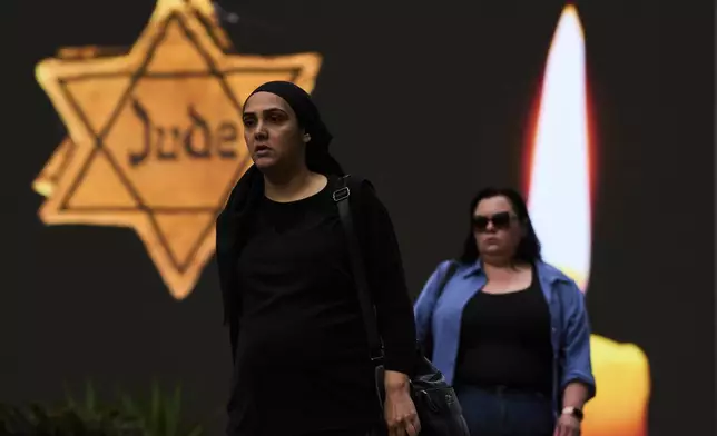 People walk next to a billboard showing a yellow Star of David that reads "Jude," Jew in German, resembling the one Jews were forced to wear in Nazi Germany, during the annual Holocaust Remembrance Day in Ramat Gan, Israel, Thursday, April 24, 2025. (AP Photo/Oded Balilty)