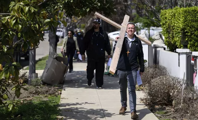 Pastor John Shaver, right, carries a cross during a Cross Walk event by the Community United Methodist Church of the Pacific Palisades, Friday, April 18, 2025, in the Pacific Palisades area of Los Angeles. (AP Photo/William Liang)