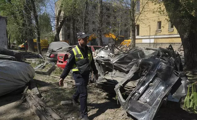 A police officer passes by remains of the cars damaged in the Russian missile attack that hit residential houses Thursday killing 12 civilians and injuring 87 in Kyiv, Ukraine, Friday, April 25, 2025. (AP Photo/Efrem Lukatsky)