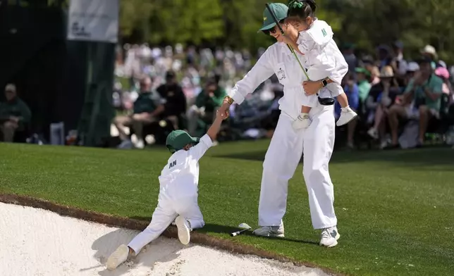 Byeong Hun An's, of South Korea, wife, Melissa, helps her son Sun-woo, 5, out of the bunker on the first hole as she holds daughter Ji-Woo, 2, during the par-3 contest at the Masters golf tournament, Wednesday, April 9, 2025, in Augusta, Ga. (AP Photo/Ashley Landis)