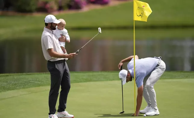Scottie Scheffler holds his child Bennett as Sam Burns removes his ball on the first hole during the par-3 contest at the Masters golf tournament, Wednesday, April 9, 2025, in Augusta, Ga. (AP Photo/Ashley Landis)