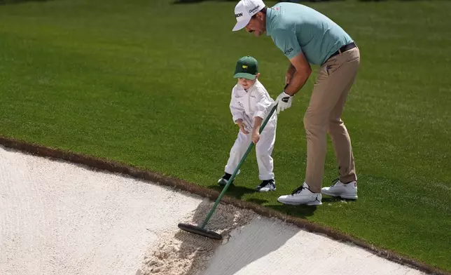 Keegan Bradley rakes the bunker with his son Cooper, 4, on the first hole during the par-3 contest at the Masters golf tournament, Wednesday, April 9, 2025, in Augusta, Ga. (AP Photo/Ashley Landis)