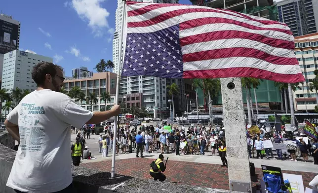 Alberto Rosales holds a U.S. flag upside down for what he calls a "symbol of crisis" during a protest against the Trump administration, Saturday, April 19, 2025, in Miami. (AP Photo/Lynne Sladky)