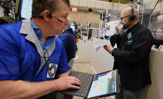 Options trader Steven Rodriguez, right, tears pages out of notepad as fellow trader Ed Nagle watches, on the floor of the New York Stock Exchange, Friday, April 11, 2025. (AP Photo/Richard Drew)