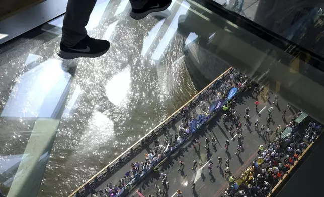 Visitors to Tower Bridge walk across the walkway as runners in the mass participation race go by during the TCS London Marathon, Sunday April 27, 2025. (Jonathan Brady/PA via AP)