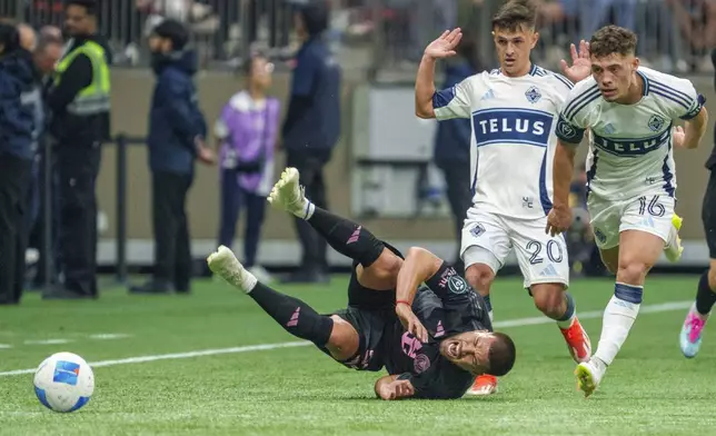 Inter Miami's Marcelo Weigandt, bottom, falls after getting tackled by Vancouver Whitecaps' Sebastian Berhalter, right, and Andres Cubas during the first half of a CONCACAF Champions Cup semifinal soccer match, in Vancouver, British Columbia, Thursday, April 24, 2025. (Christopher Morris/The Canadian Press via AP)