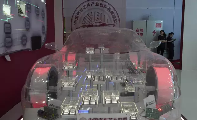 Workers stand near a model demonstrating products from the China Automotive Chip Alliance during the Shanghai auto show on Thursday, April 24, 2025. (AP Photo/Ng Han Guan)