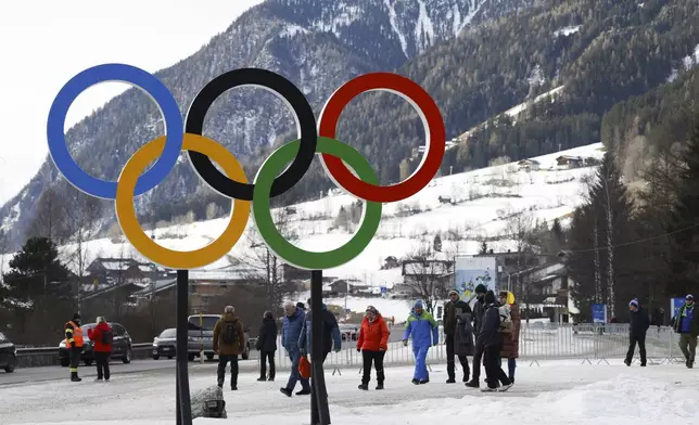 People walk near Olympic rings near the village of Anterselva where the Biathlon will take place during the Milan Cortina 2026 Winter Olympics, in northern Italy, Saturday, Jan. 25, 2025. (AP Photo/Alessandro Trovati)