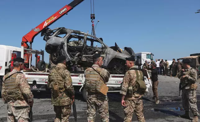 Lebanese army soldiers stand guard as workers use a crane to remove a charred car that was hit by an Israeli strike, in the southern coastal town of Ghazieh, Lebanon, Friday, April 18, 2025. (AP Photo/Mohammed Zaatari)