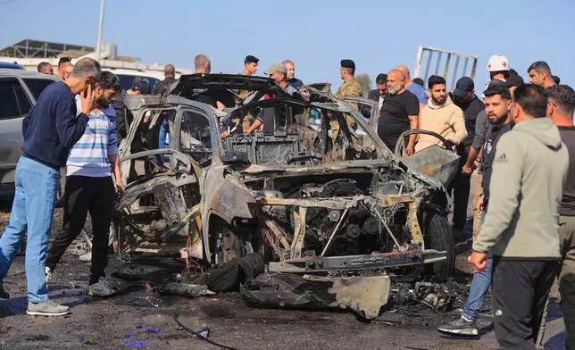 People gather near a charred car that was hit by an Israeli strike, in the southern coastal town of Ghazieh, Lebanon, Friday, April 18, 2025. (AP Photo/Mohammed Zaatari)