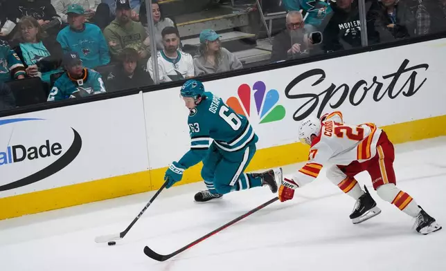 San Jose Sharks center Zack Ostapchuk, left, moves with the puck as Calgary Flames right wing Matt Coronato (27) attempts to defend during the second period of an NHL hockey game in San Jose, Calif., Monday, April 7, 2025. (AP Photo/Minh Connors)