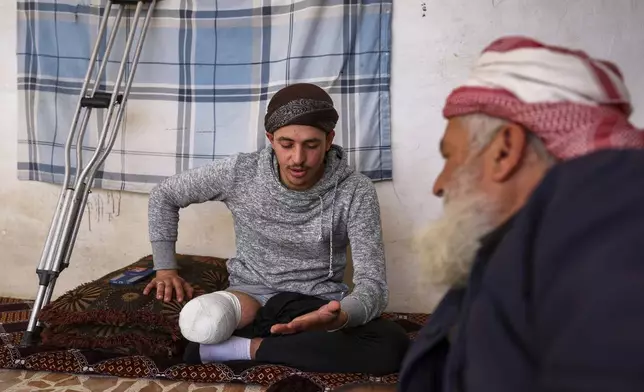 Suleiman Khalil, 21, who lost his leg in a landmine explosion while harvesting olives with his friends in a field, talks with his father at their home in the village of Qaminas, east of Idlib, Syria, Wednesday, April 9, 2025. (AP Photo/Ghaith Alsayed)