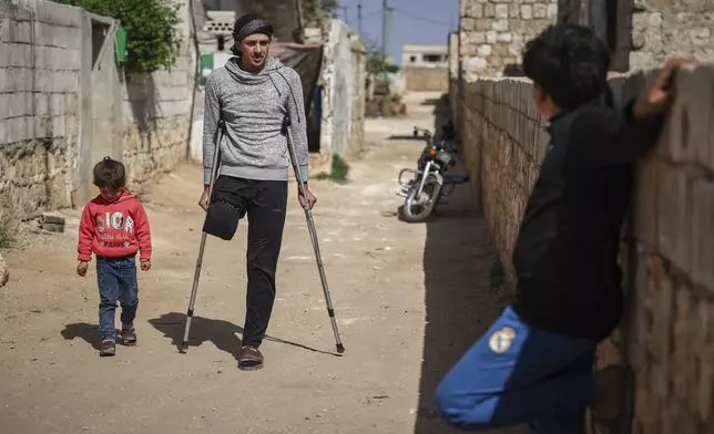 Suleiman Khalil, 21, who lost his leg in a landmine explosion while harvesting olives with his friends in a field, walks outside his home in the village of Qaminas, east of Idlib, Syria, Wednesday, April 9, 2025. (AP Photo/Ghaith Alsayed)