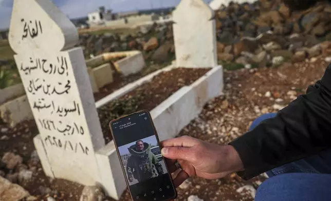 Salah Swed , 28, holds a cellphone showing a picture of his brother Mohammed, killed while attempting to dismantle a landmine, as he visits his grave in their village of Kafr Nabl, south of Idlib, Syria, Monday, April 14, 2025.(AP Photo/Ghaith Alsayed)
