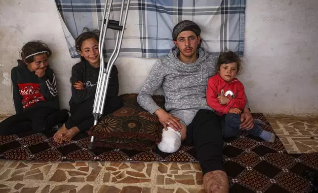 Suleiman Khalil, 21, who lost his leg in a landmine explosion while harvesting olives with his friends in a field, poses for a pictures with his siblings from left to right, Sakina, 8, Nahla, 9, and Aya, 5, at his home in the village of Qaminas, east of Idlib, Syria, Wednesday, April 9, 2025. (AP Photo/Ghaith Alsayed)
