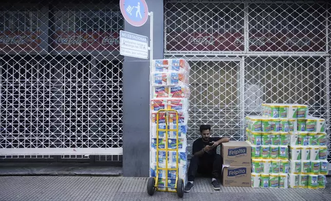 A worker sits outside a supermarket waiting for the store to open to deliver toilet paper in Buenos Aires, Argentina, Monday, April 14, 2025. (AP Photo/Natacha Pisarenko)