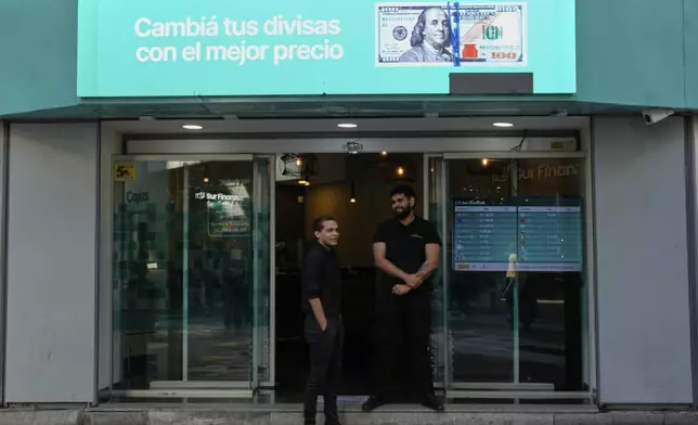 Workers at a currency exchange house stand at the store's entrance in Buenos Aires, Argentina, Monday, April 14, 2025. (AP Photo/Natacha Pisarenko)