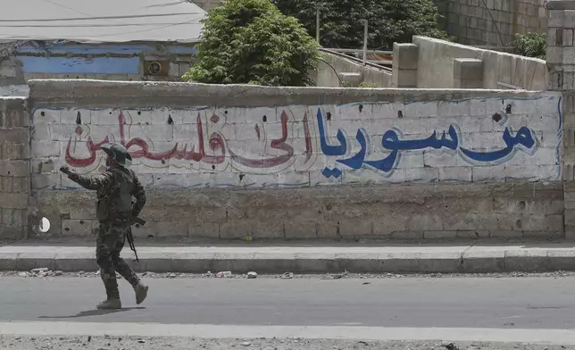 A Syrian government security forces gunman passes in front of an Arabic graffiti that reads "From Syria to Palestine", at one of Jaramana suburb entrances, after clashes erupted in the area between members of the minority Druze sect and pro-government fighters, in the southern suburb of Jaramana, Damascus, Syria, Wednesday, April 30, 2025. (AP Photo/Omar Sanadiki)