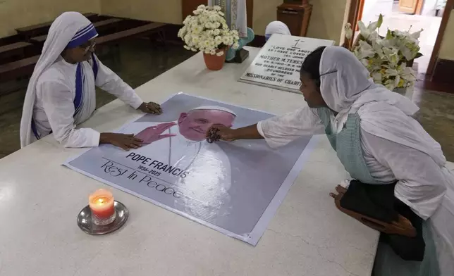 Catholic nuns of the Missionaries of Charity, the order founded by Saint Teresa, touch a portrait of Pope Francis, as they pray on the saint's tomb in Kolkata, India, Tuesday, April 22, 2025. (AP Photo/Bikas Das)
