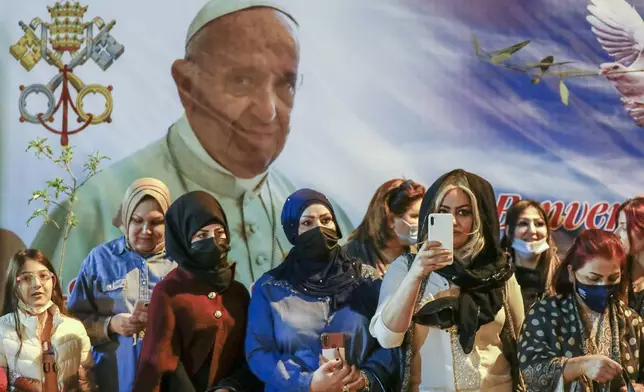 FILE.- Women wait outside the Chaldean Cathedral of Saint Joseph, in Baghdad, Iraq, Saturday, March 6, 2021, where Pope Francis, depicted on a giant poster at their back, is concelebrating a mass. (AP Photo/Andrew Medichini,File)
