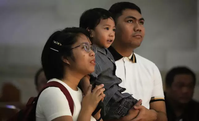 A family says a prayer in front of the portrait of the late Pope Francis at the Manila Cathedral in the country's capital Manila, Philippines Tuesday, April 22, 2025. (AP Photo/Aaron Favila)