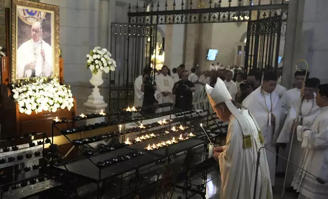 Philippine Cardinal Jose Advincula, foreground, lights a candle in front of a portrait of the late Pope Francis at the Manila Cathedral in the country's capital Manila, Philippines Tuesday, April 22, 2025. (AP Photo/Aaron Favila)