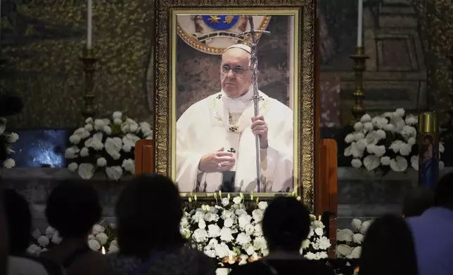 Catholics lights candles in front of a portrait of the late Pope Francis at the Manila Cathedral in Manila, Philippines Tuesday, April 22, 2025. (AP Photo/Aaron Favila)