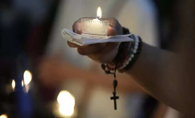 A man lights a candle in front of a portrait of the late Pope Francis at the Manila Cathedral in the country's capital, Philippines Tuesday April 22, 2025. (AP Photo/Aaron Favila)