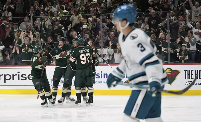 Minnesota Wild center Joel Eriksson Ek (14), middle, celebrates with teammates after scoring a goal as San Jose Sharks defenseman Henry Thrun (3), foreground, skates across the ice during the third period of an NHL hockey game, Wednesday, April 9, 2025, in St. Paul, Minn. (AP Photo/Abbie Parr)